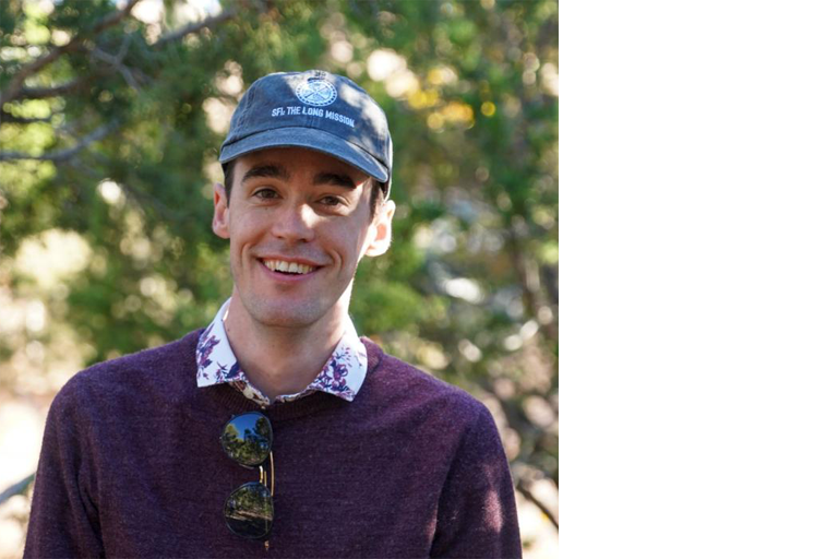 headshot of Jeffrey Lockhart, wearing a blue basecall hat with trees in the background