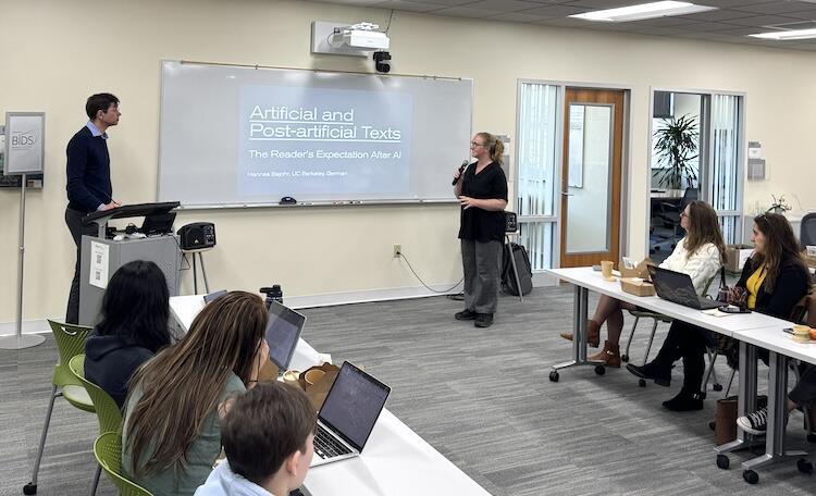 Hannes Bajohr stands next to a podium and a screen, and Kirstie Whitaker holds a microphone