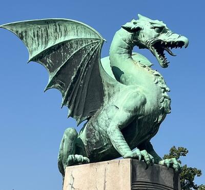 a large bronze sculpture of a dragon, wings up and mouth open, sitting on a rectangular stone base
